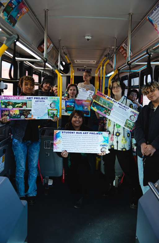 Student artists who designed the MMT bus wraps take a picture together on a bus holding signs promoting the project.