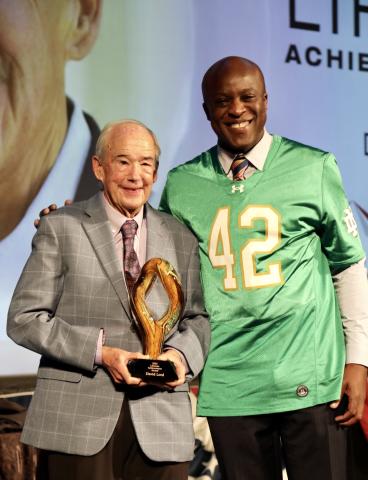 Mayor Yemi and David Lord take a photo together with Lord's Lifetime Achievement Award on stage at the 2025 State of the City Event.