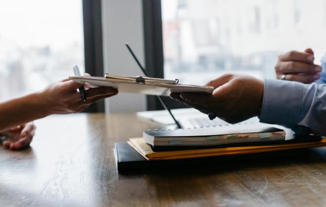 Two people passing a clipboard to each other over a table